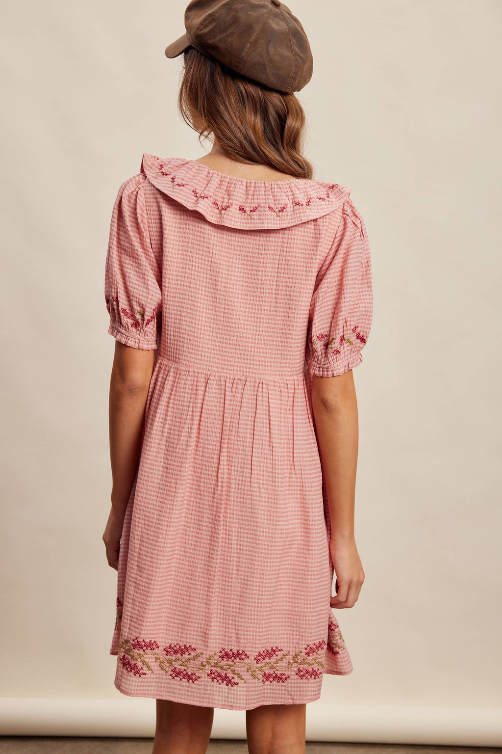Woman wearing a pink checkered dress with floral embroidery on a beige background
