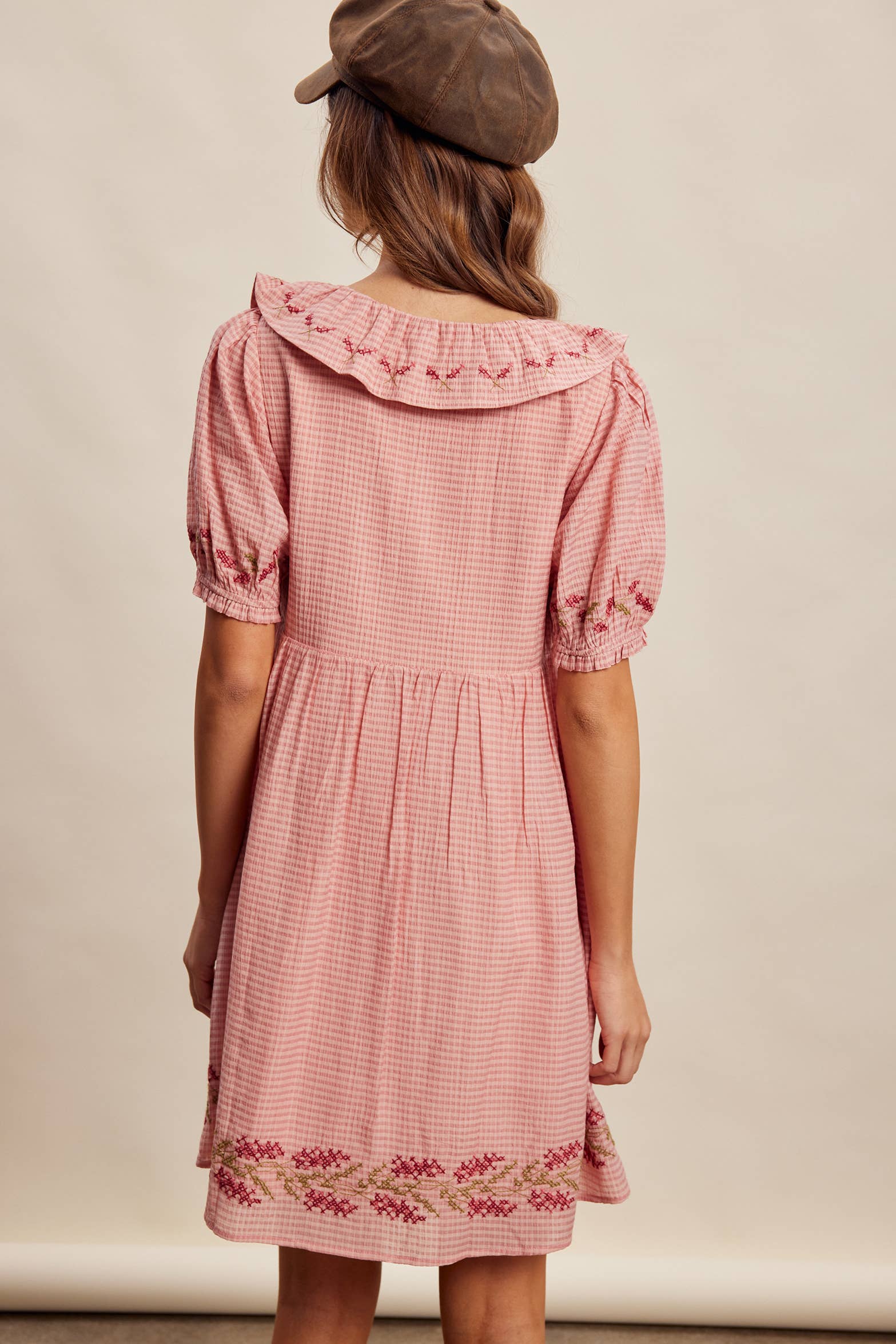Woman wearing a pink checkered dress with floral embroidery on a beige background