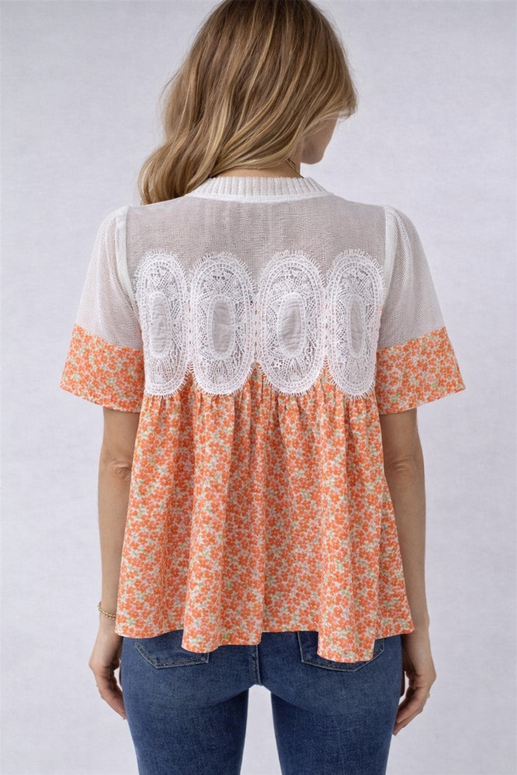 Woman wearing a floral blouse with lace details on a plain background