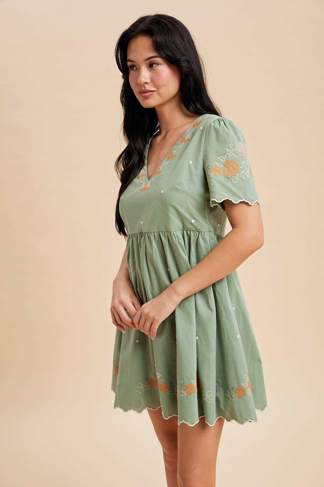 Woman wearing a green dress with floral embroidery on a beige background