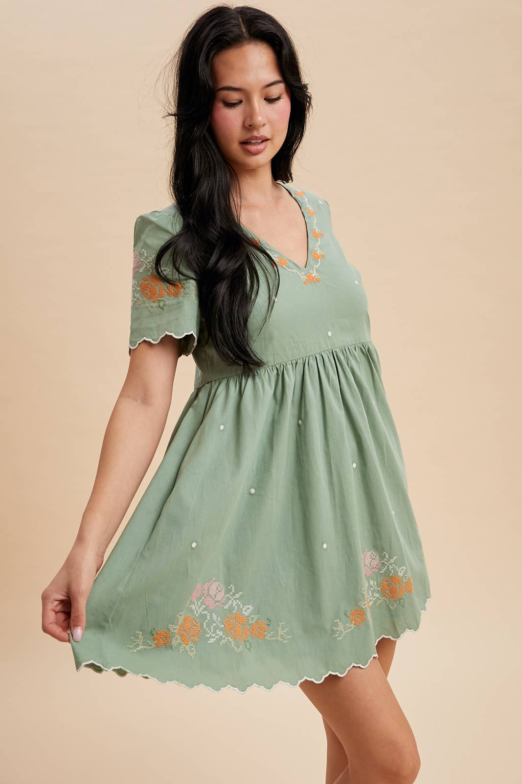 Woman wearing a green dress with floral embroidery on a beige background