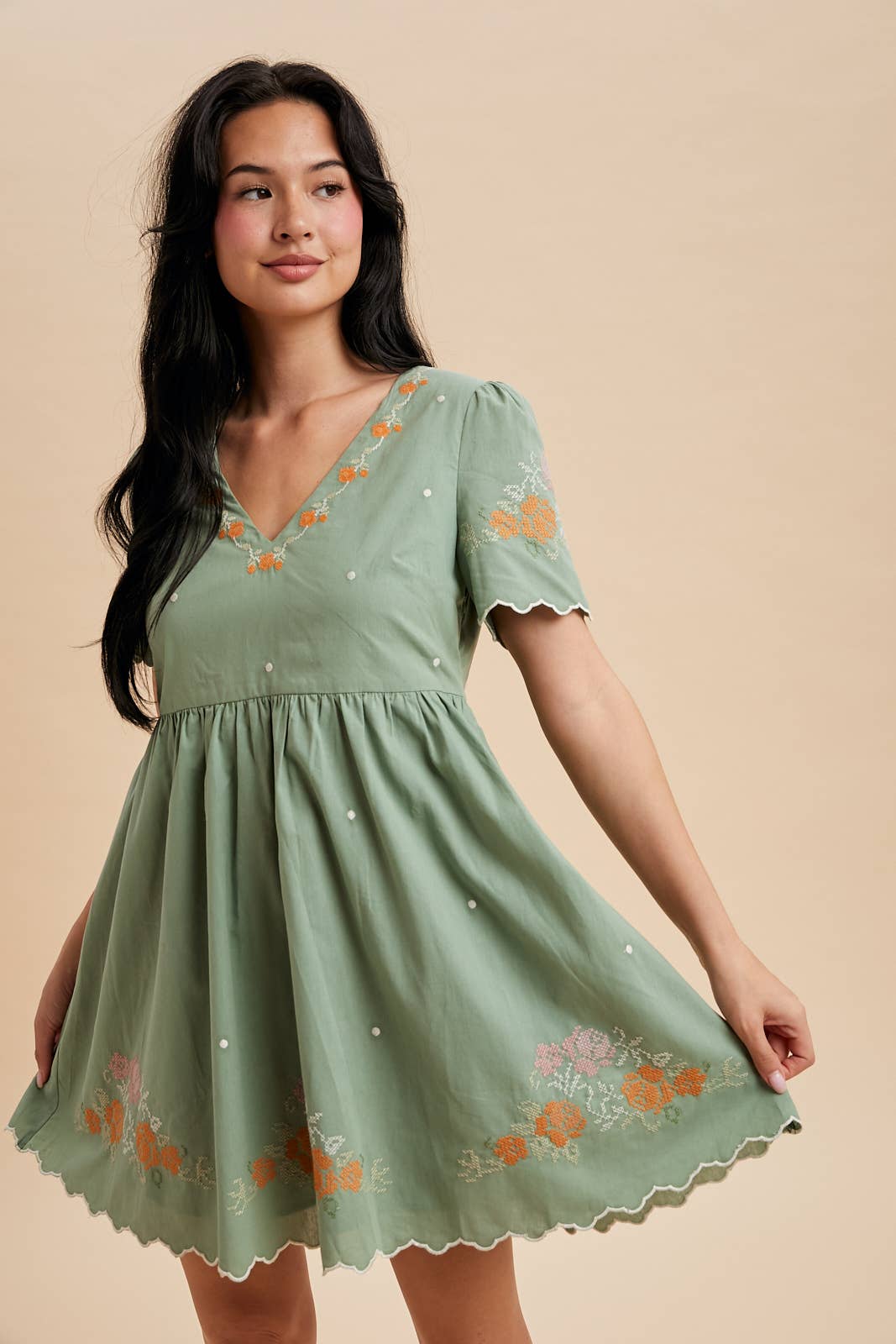 Woman wearing a green dress with floral embroidery on a beige background