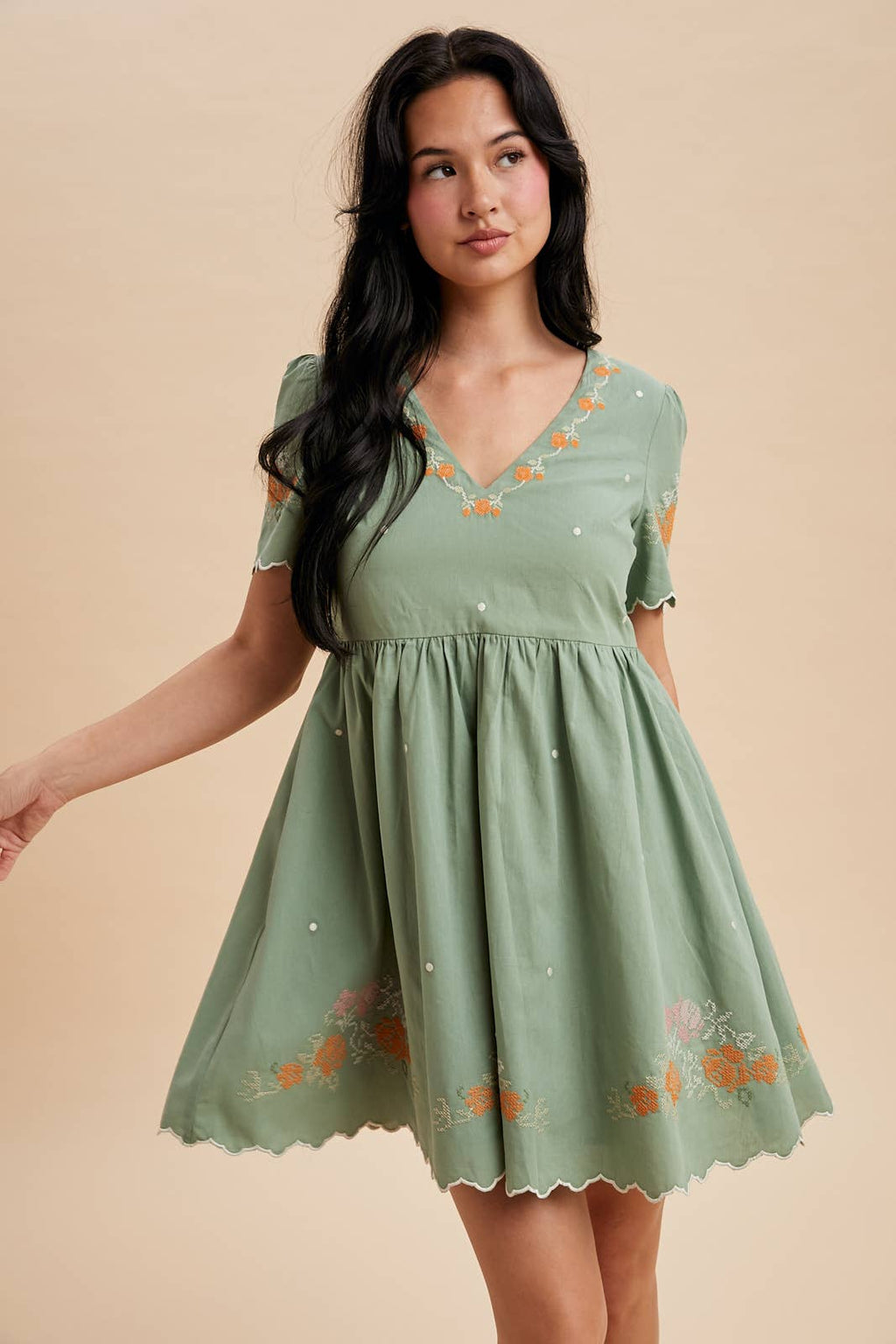 Woman wearing a green dress with floral embroidery on a beige background