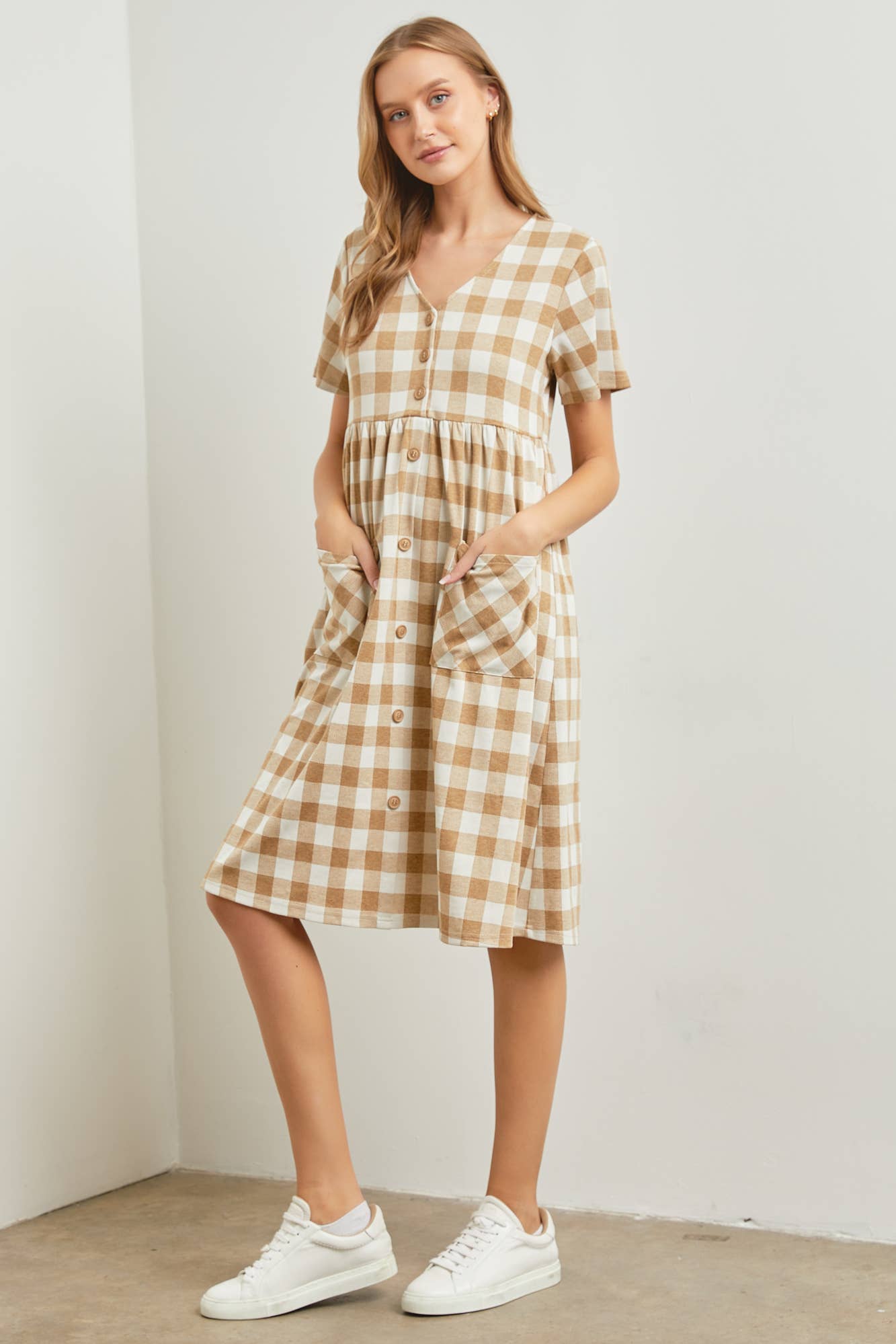 Woman wearing a checkered dress with white sneakers against a plain background
