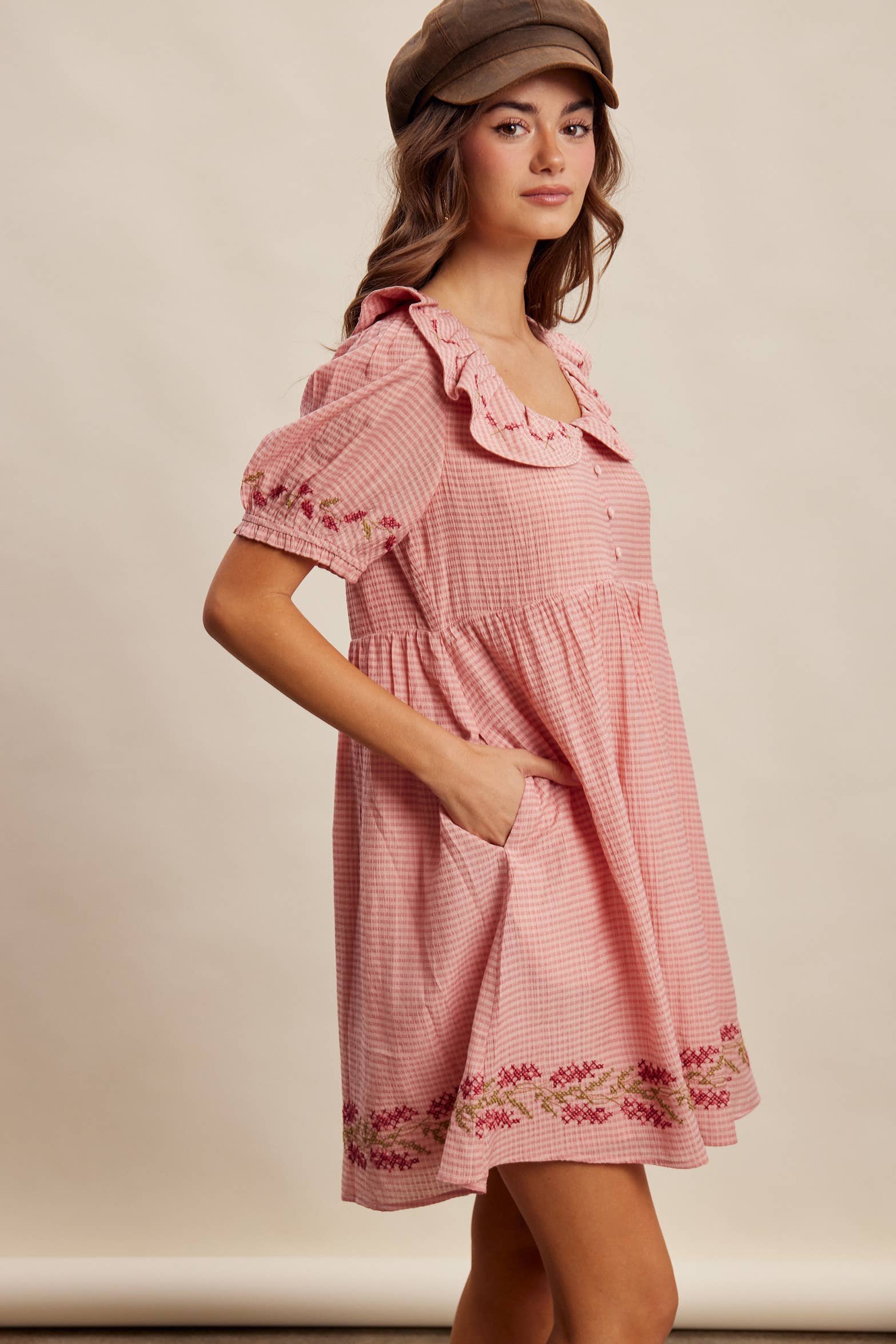 Woman wearing a pink checkered dress with floral embroidery on a plain background